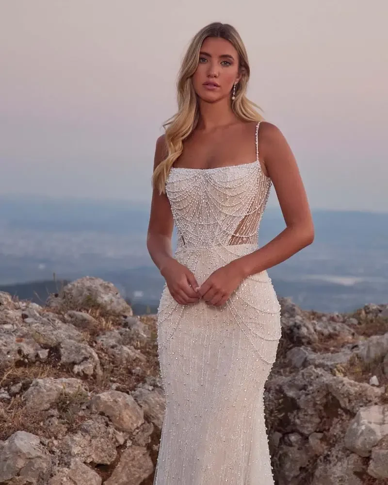 Model is wearing a beaded bridal gown with pearls and spaghetti straps