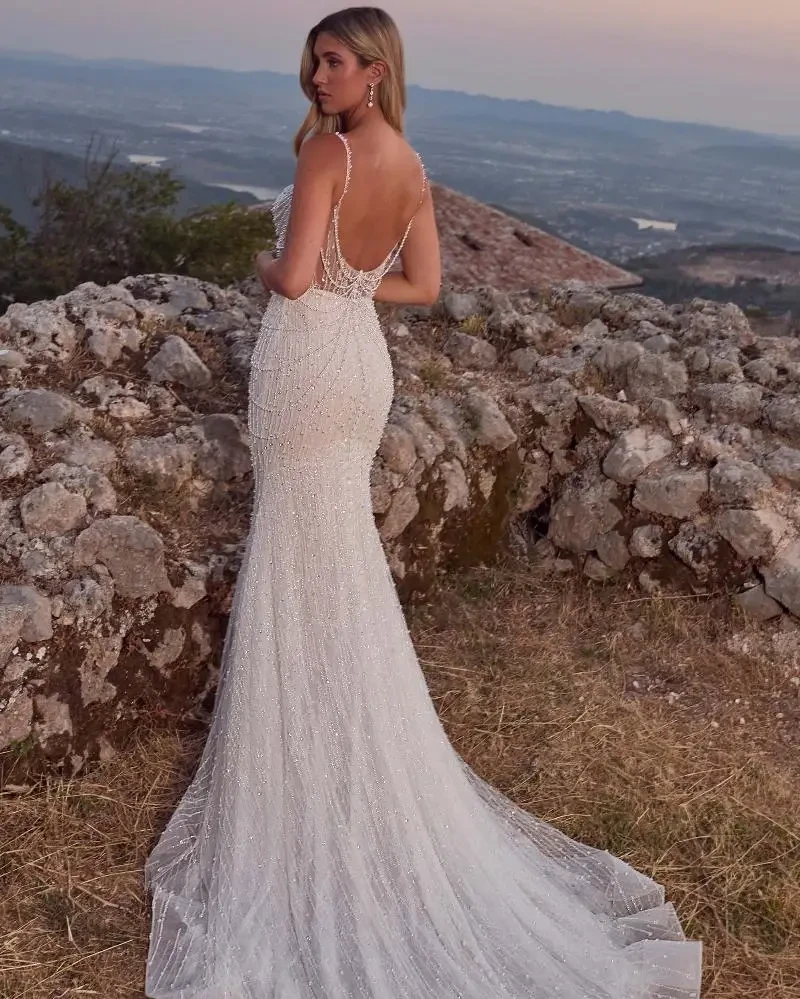 Model is wearing a beaded bridal gown with pearls and spaghetti straps