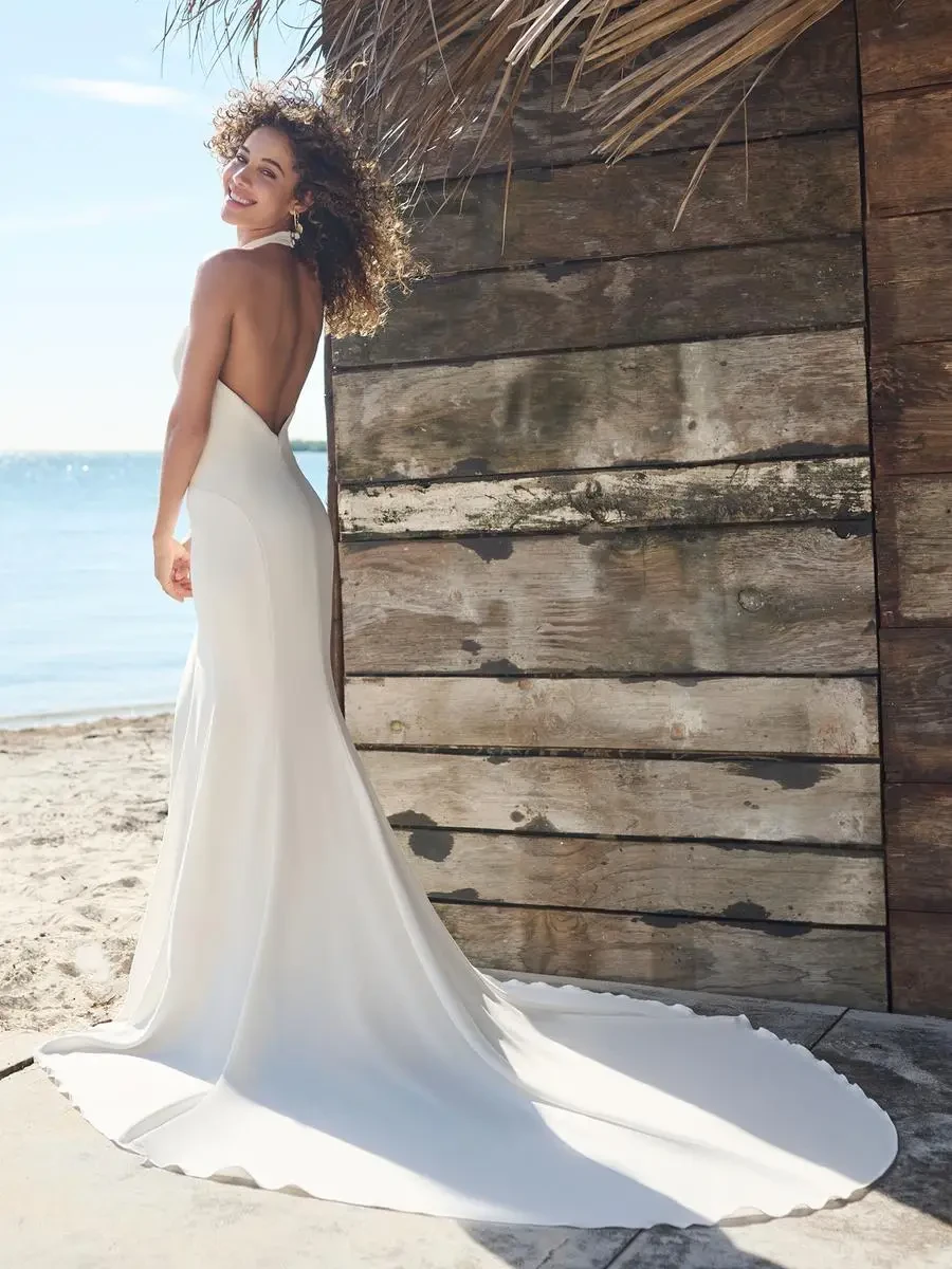 Model is wearing a crepe halter neckline wedding dress with an open back and side slit