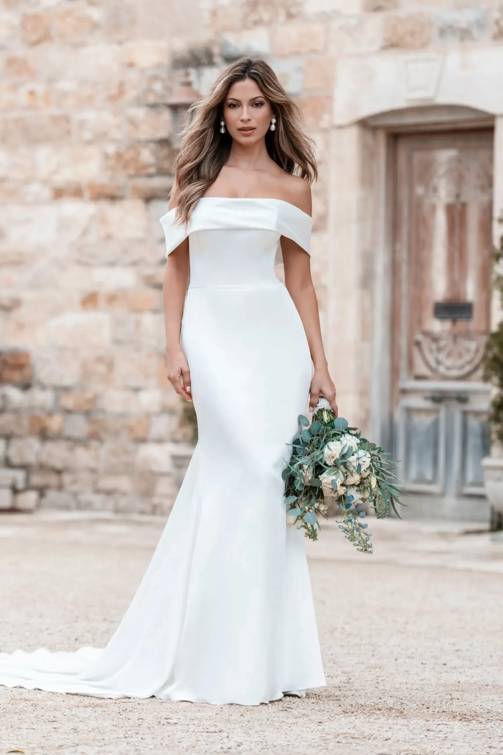 Model is wearing a chic off-shoulder satin sheath dress accented with a flirty bow at the back.