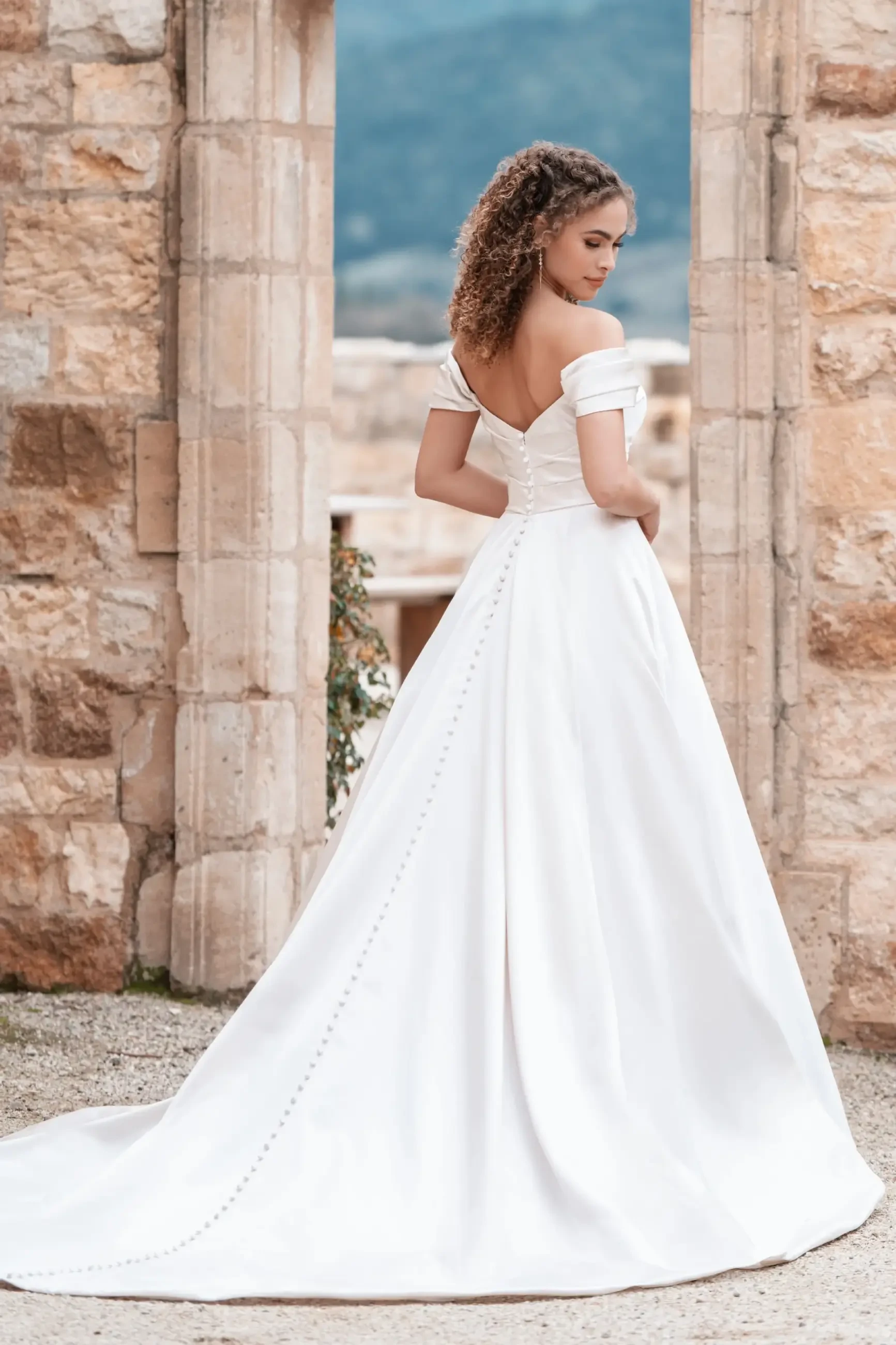 Model is wearing an elegant satin ballgown with ruched detailing, a sweetheart neckline, and off-shoulder straps.