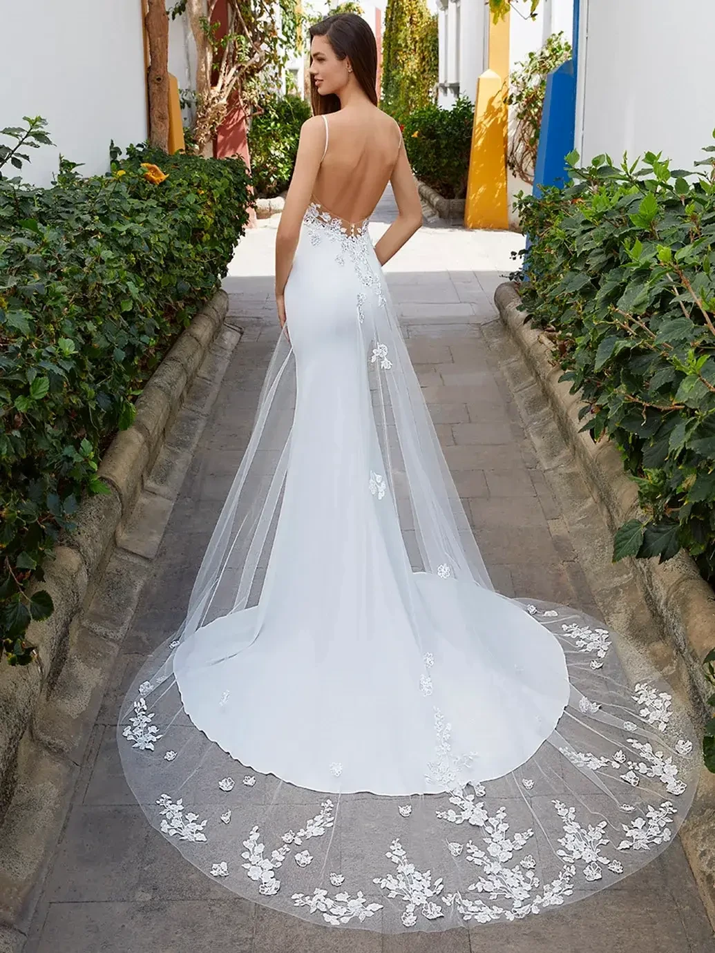 Model is wearing a lightweight stretch georgette gown with thin spaghetti straps, a modern square neckline, and a low illusion back detailed in delicate floral lace.