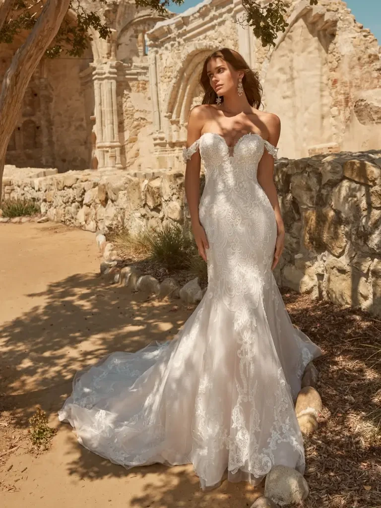 Model is wearing a fitted mermaid bridal gown with an elegant off-the-shoulder neckline and structured bodice.