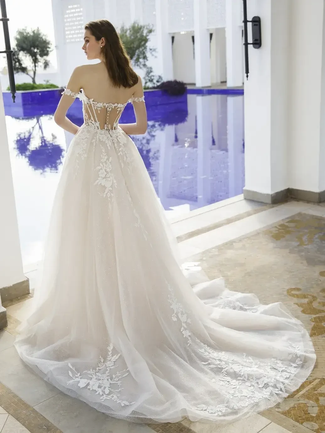 Model is wearing a glitter tulle A-line bridal gown with a floral lace corset bodice, sweetheart neckline, detachable off-the-shoulder straps, and a sparkly chapel train.