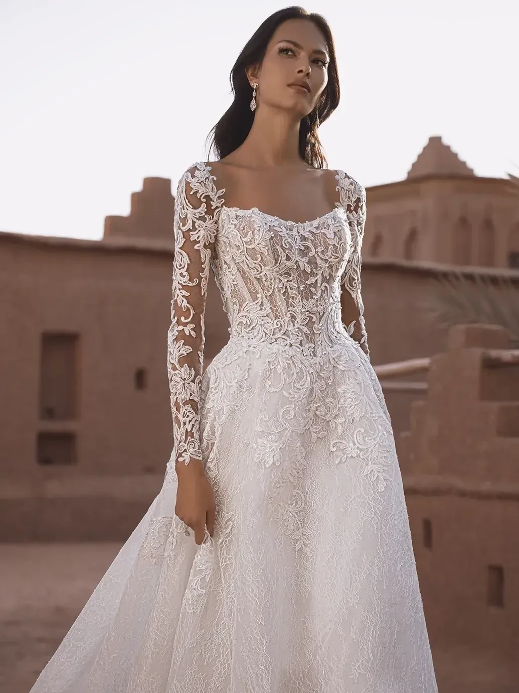 model is wearing a lace long sleeve a-line bridal gown with a bold train