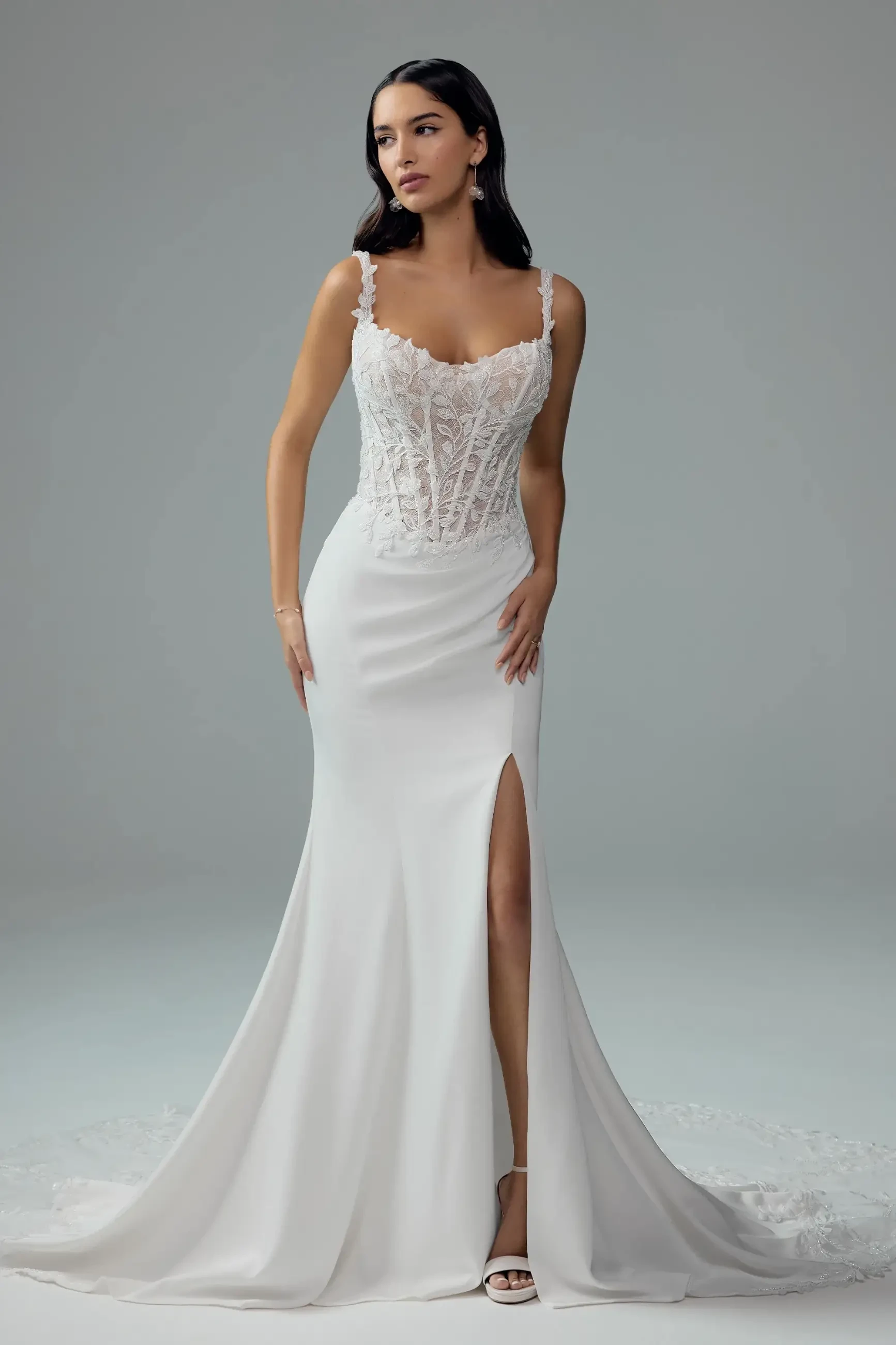 Model is wearing a fit-and-flare satin crepe wedding dress with a thigh-high slit, floral lace corset bodice, lace straps, and a deep V-back with fabric-covered buttons and a lace train.
